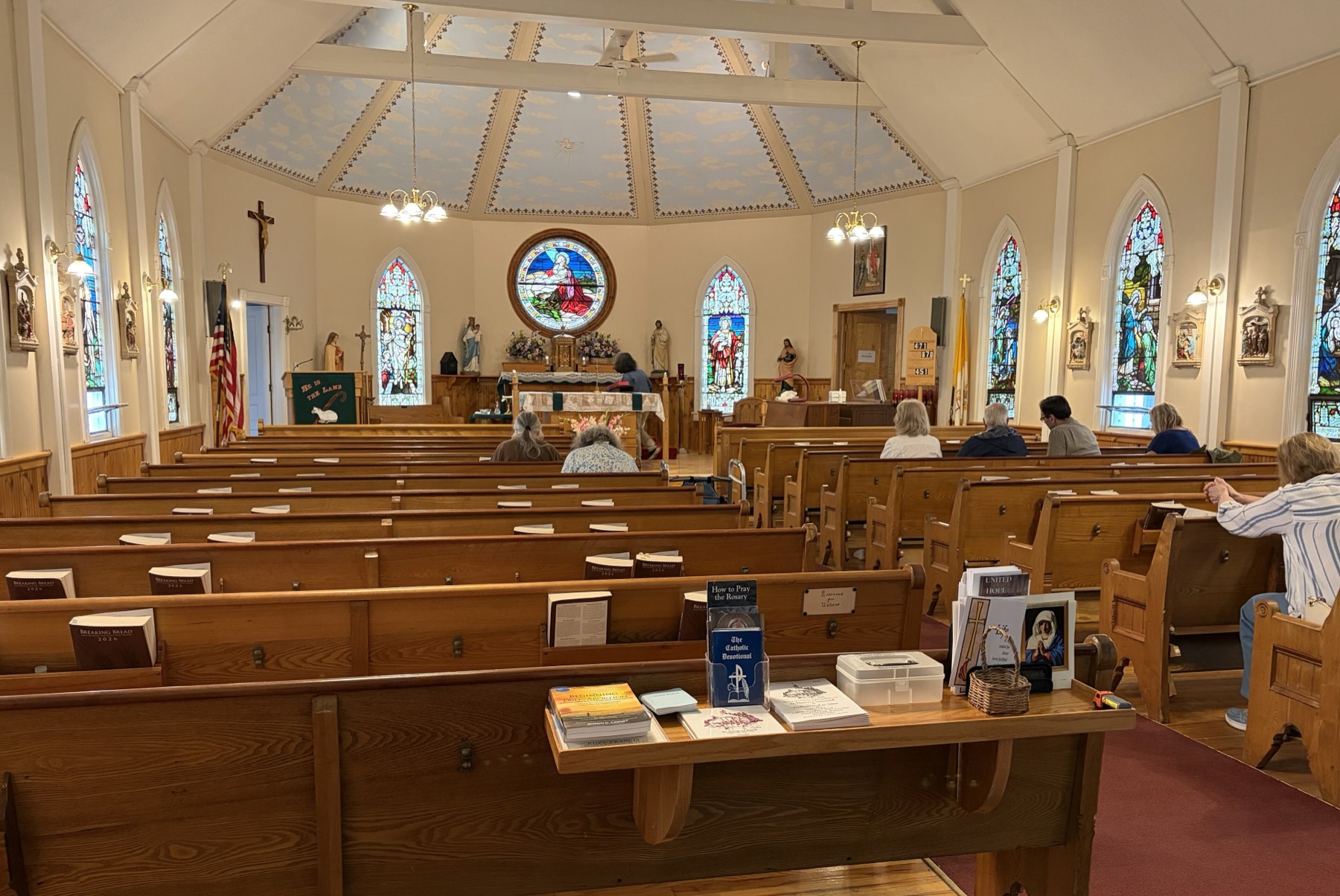The bright interior of St. Henry's Catholic Church, with stained glass, a crucifix, altar, and pews prepared for worship.